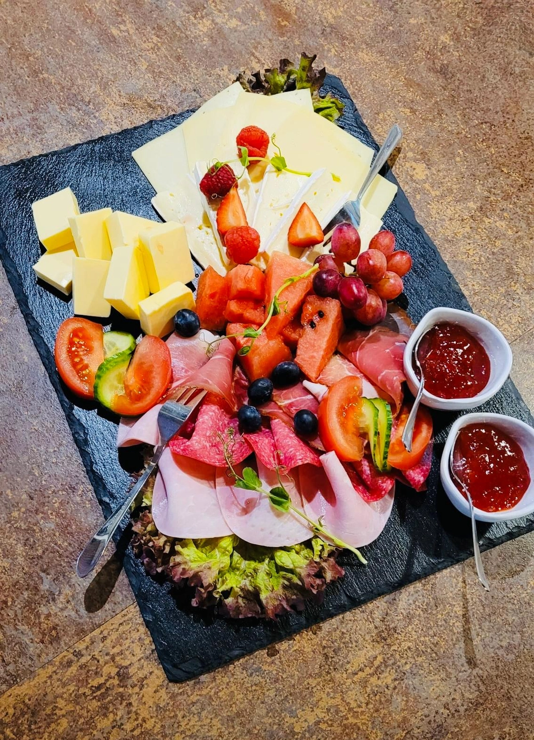 Apfelbaum – Restaurant – Dieses Bild zeigt eine wunderschön angerichtete Wurst- und Käseplatte mit verschiedenen Speisen, serviert auf einer Schieferplatte.