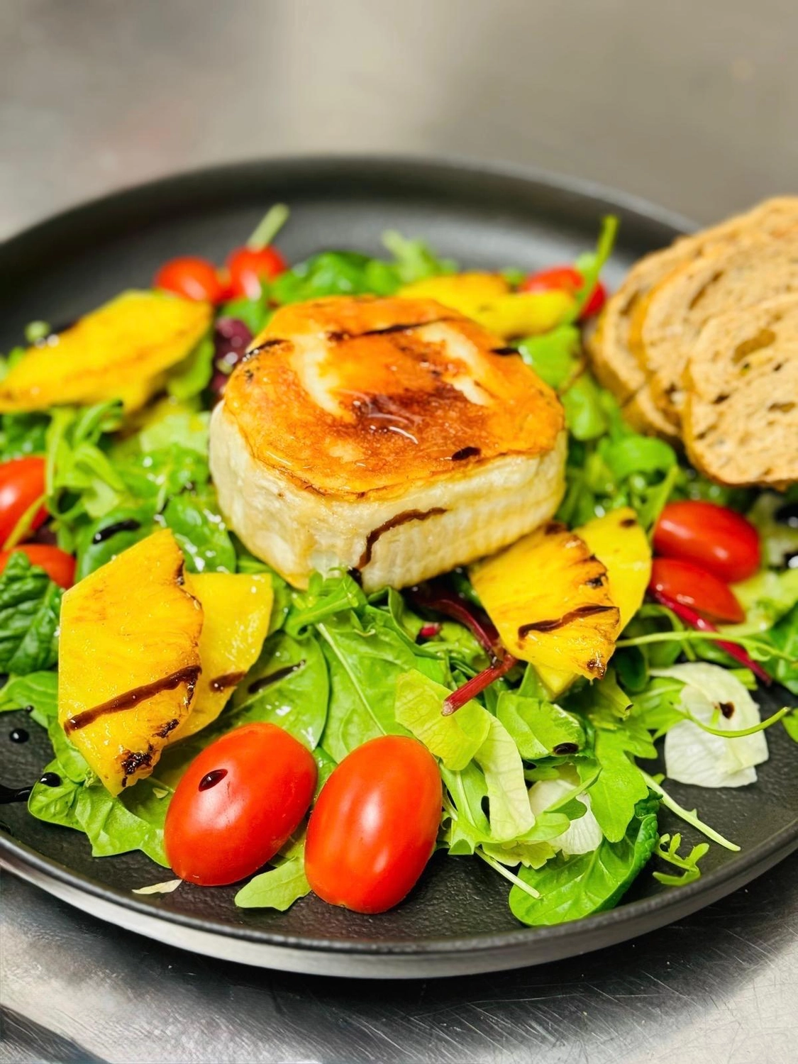 Apfelbaum – Restaurant – Dieses Bild zeigt einen klassischen Ziegenkäsesalat mit einem großen Stück gegrilltem oder gratiniertem Ziegenkäse, überzogen mit Balsamico-Glasur und serviert auf einem Salatbett.
