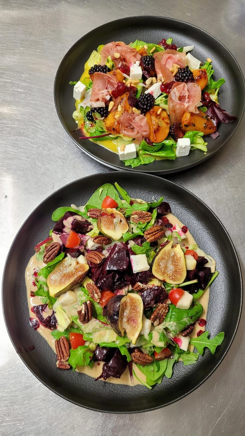 Apfelbaum – Restaurant – Das Bild zeigt einen Blutmondsalat, der aus einer Mischung aus Blattsalaten, Brombeeren, Feigen, cremigem Ziegenkäse und Prosciutto besteht und typischerweise mit einer Vinaigrette angemacht wird.