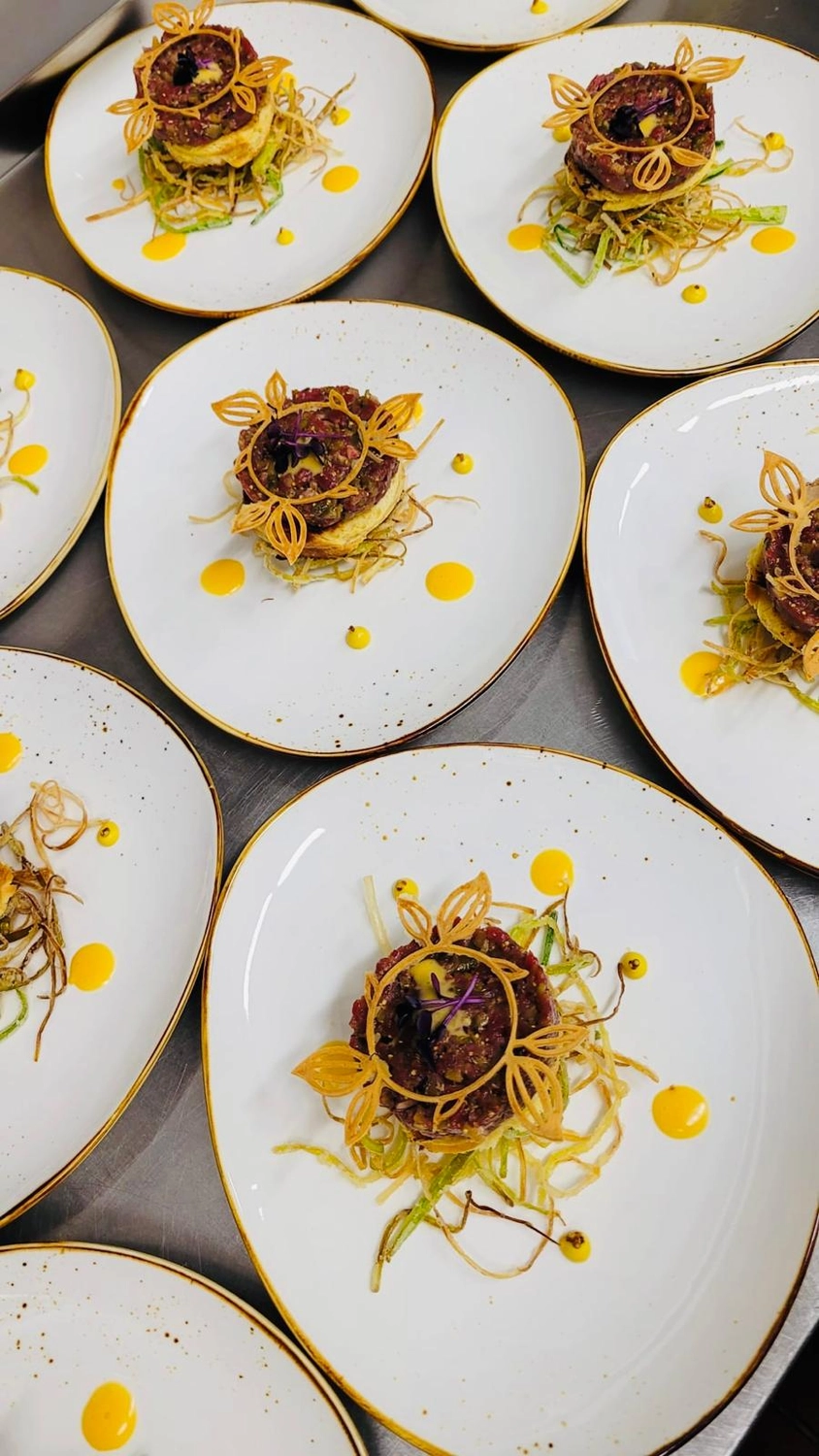 Apfelbaum – Restaurant – Dieses Bild zeigt ein wunderschön angerichtetes Gericht, wahrscheinlich aus einem Gourmetrestaurant oder von einem privaten Catering-Event, bestehend aus Thunfisch-Tatar oder einem ähnlichen rohen Meeresfrüchtegericht, garniert mit kunstvoll frittierten Gemüsestreifen.